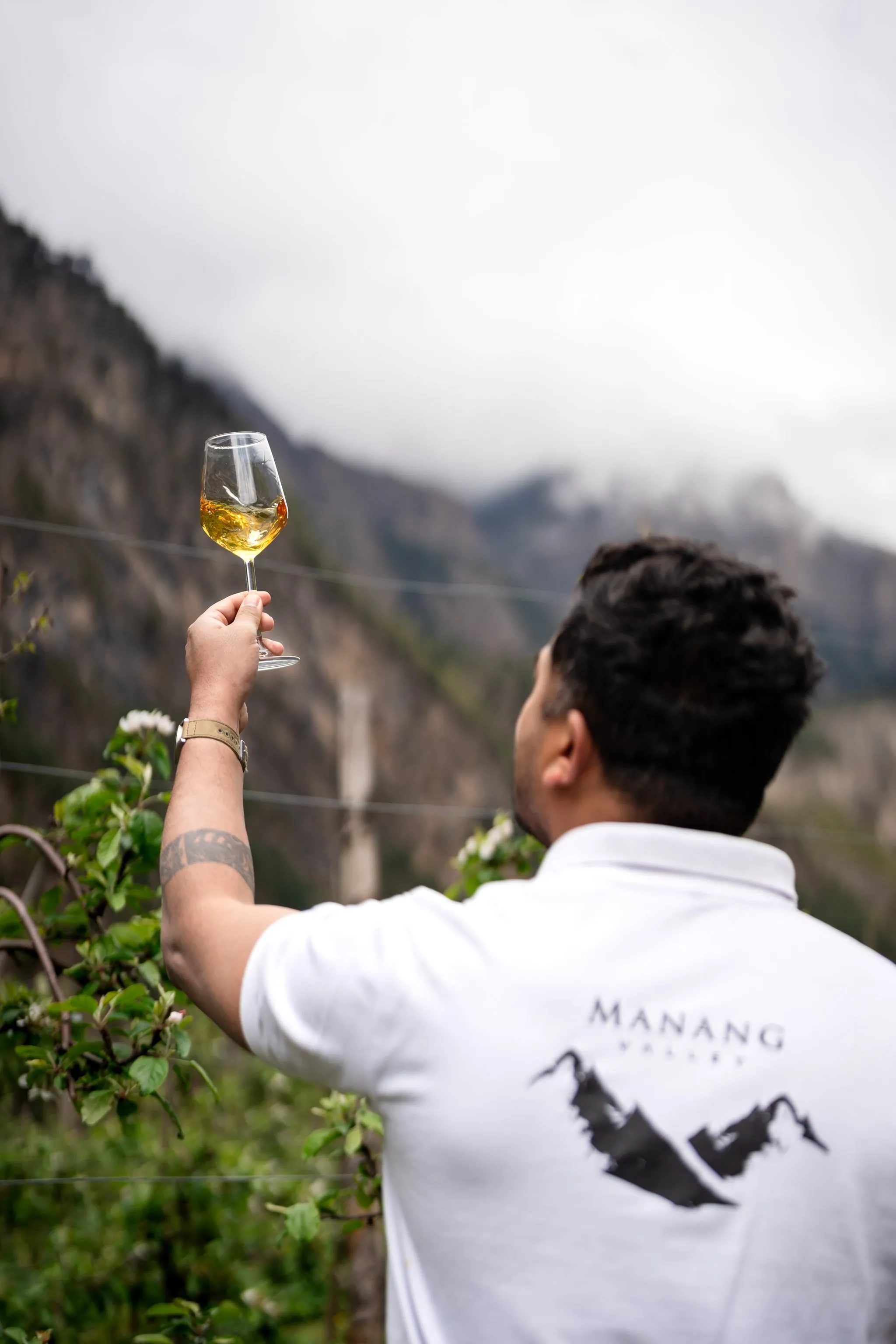 A man raises a glass of Manang Valley wine towards the mountains