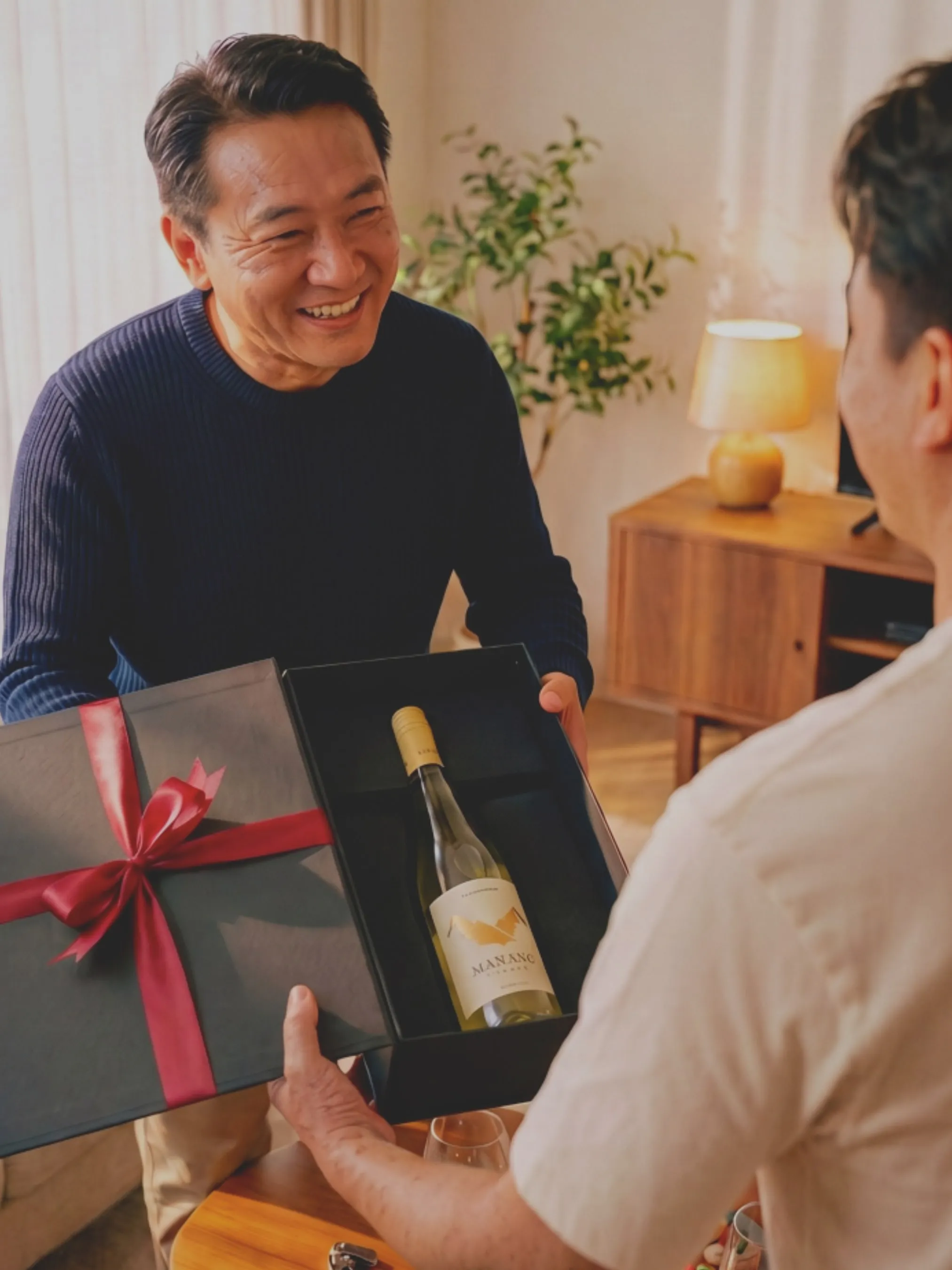 A man smiling as he is handed a gift box of wine